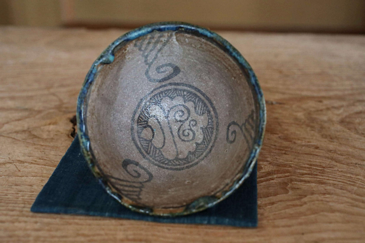 An old, weathered ceramic bowl with a decorative design on its surface, resting on a wooden surface.