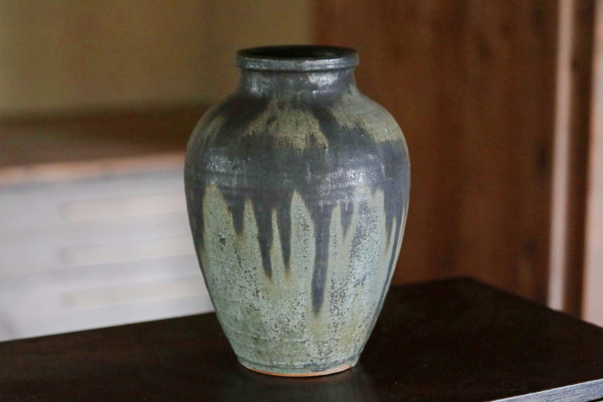 A large, gray ceramic vase with a textured surface sits on a dark surface.