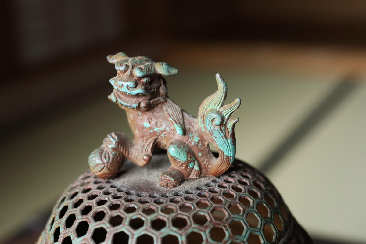 a small, intricately designed metal figurine of a lion or mythical creature, sitting atop a metal mesh or perforated structure.