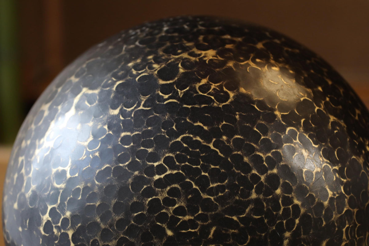 A close-up image of a black, textured surface with a pattern of small circles or dots, possibly resembling a ceramic or glass object.