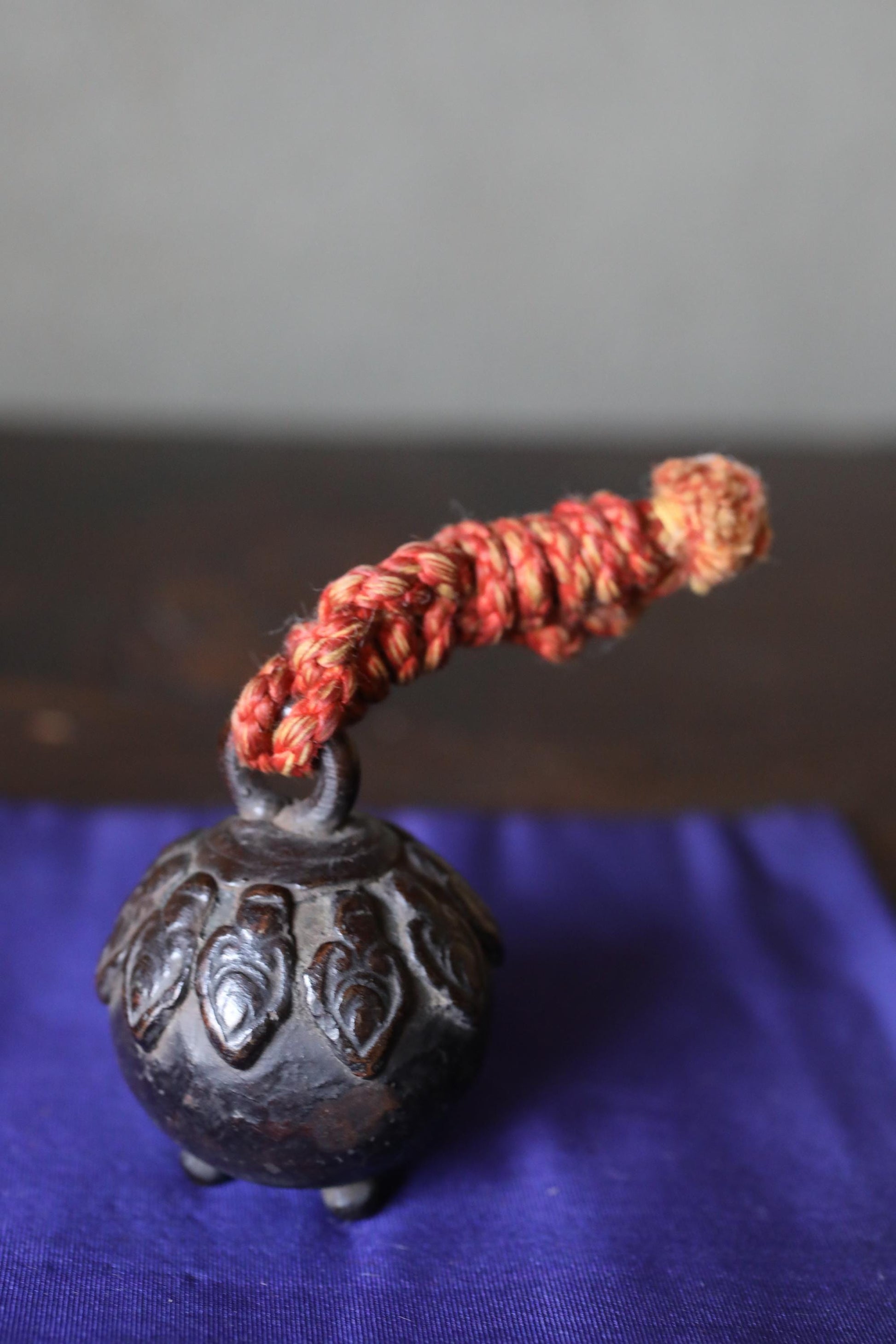A small, ornate metal bell with a red string or cord attached to it, resting on a blue cloth.