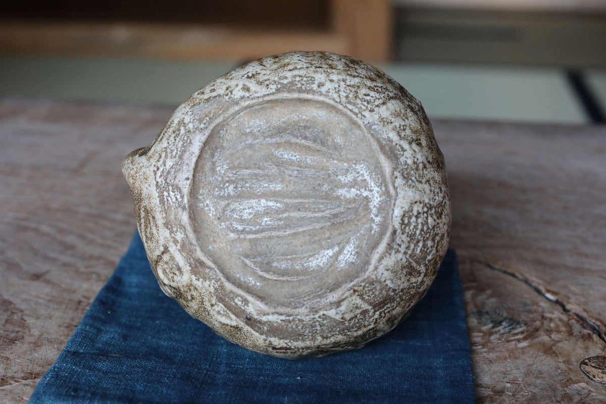 A close-up image of a ceramic object with a textured surface, resting on a blue cloth.