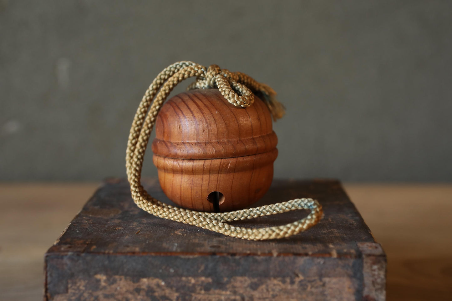 A wooden bell with a rope hanging from it, sitting on a wooden surface.
