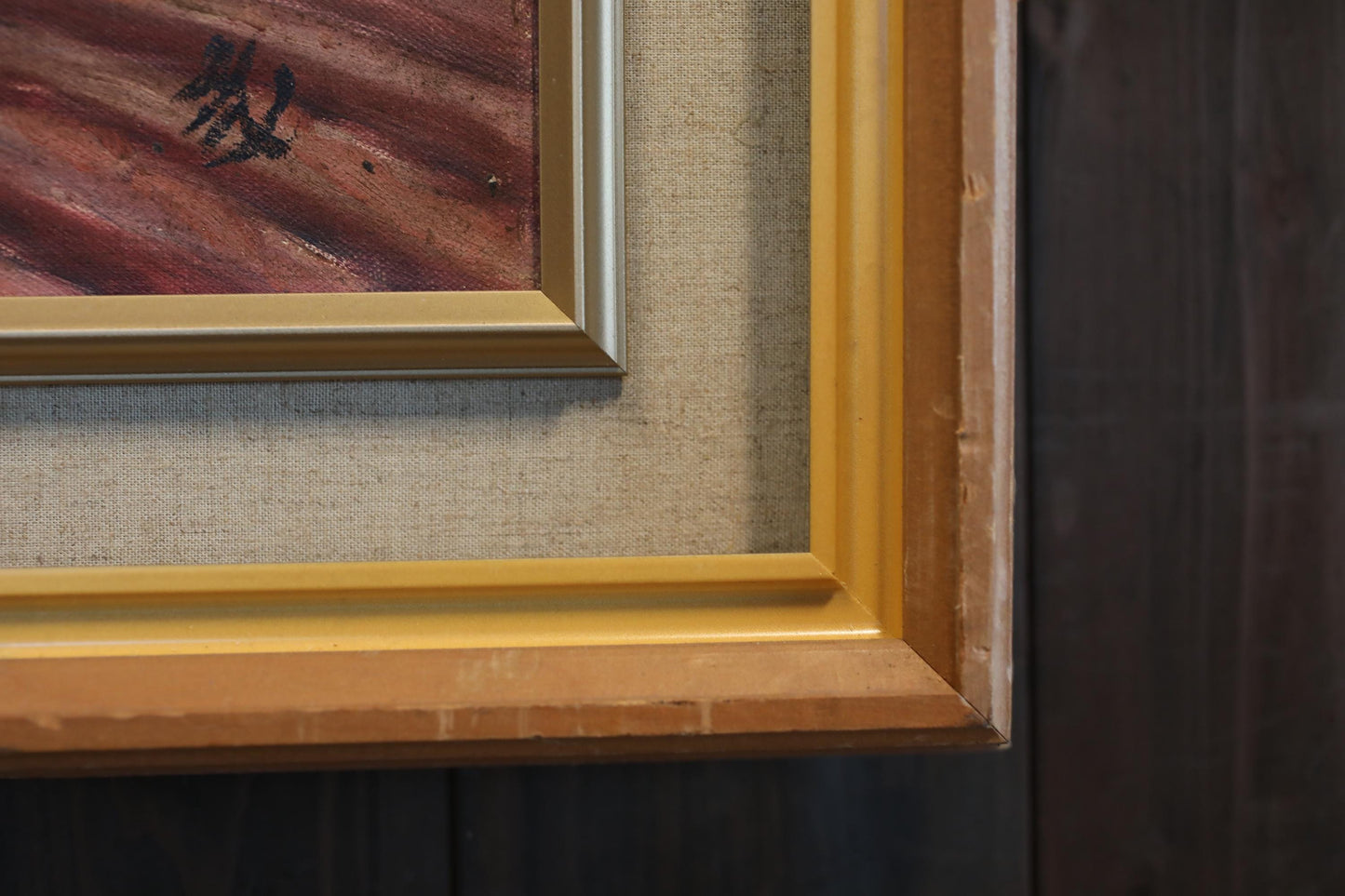 a close-up view of a framed painting with a wooden frame, set against a dark background.