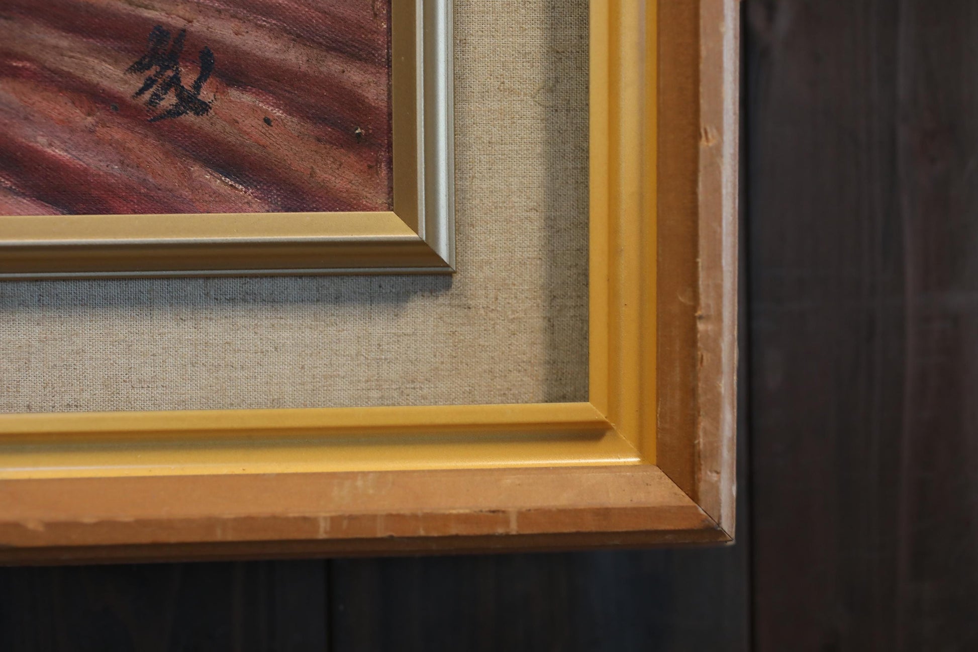 a close-up view of a framed painting with a wooden frame, set against a dark background.
