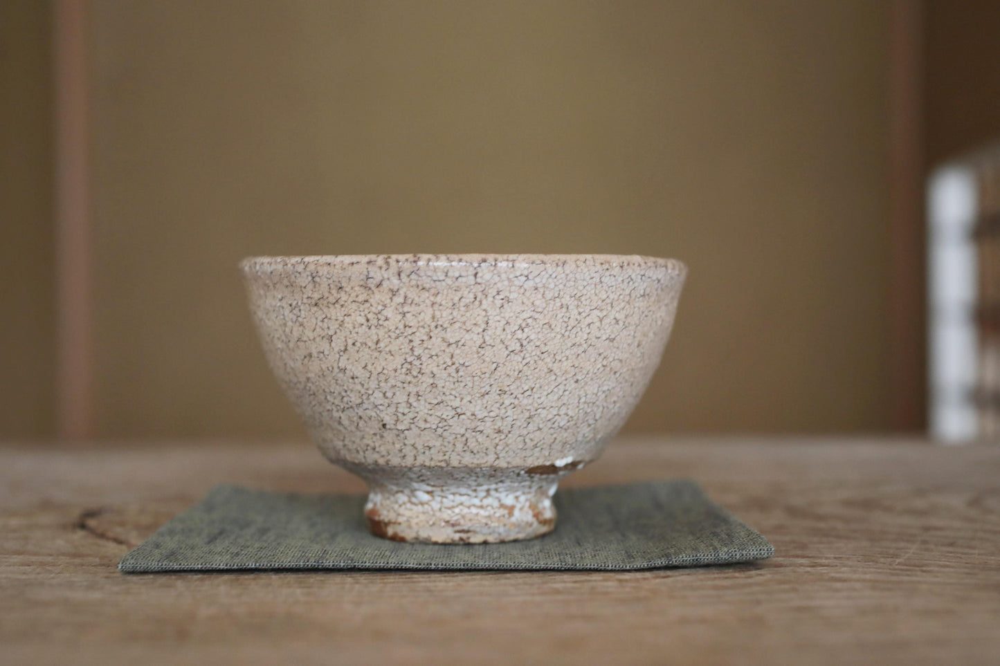 A white ceramic bowl with a speckled texture sits on a green cloth on a wooden surface.