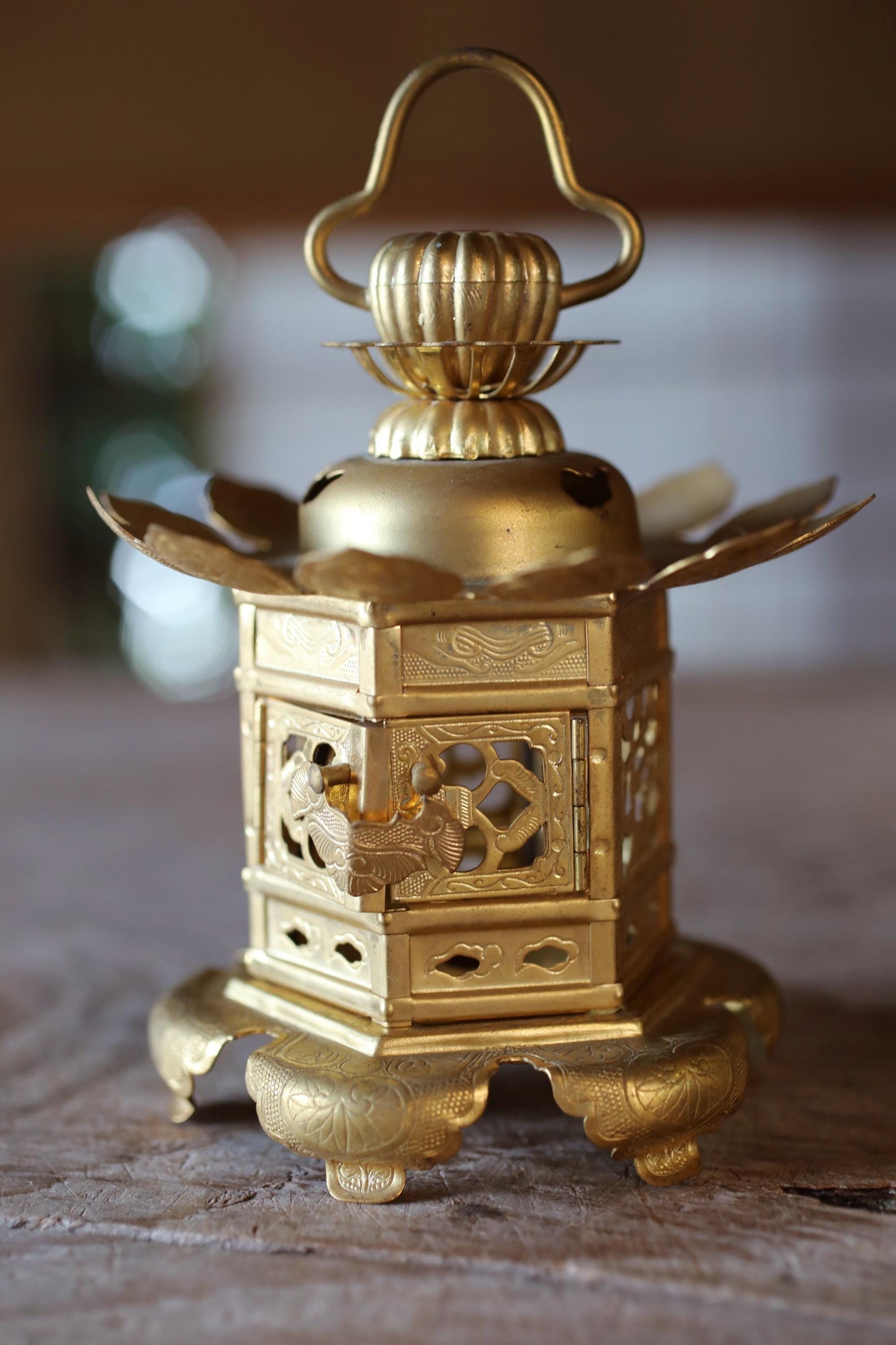 A golden, ornate lantern with intricate designs and a pointed top sits on a wooden surface.