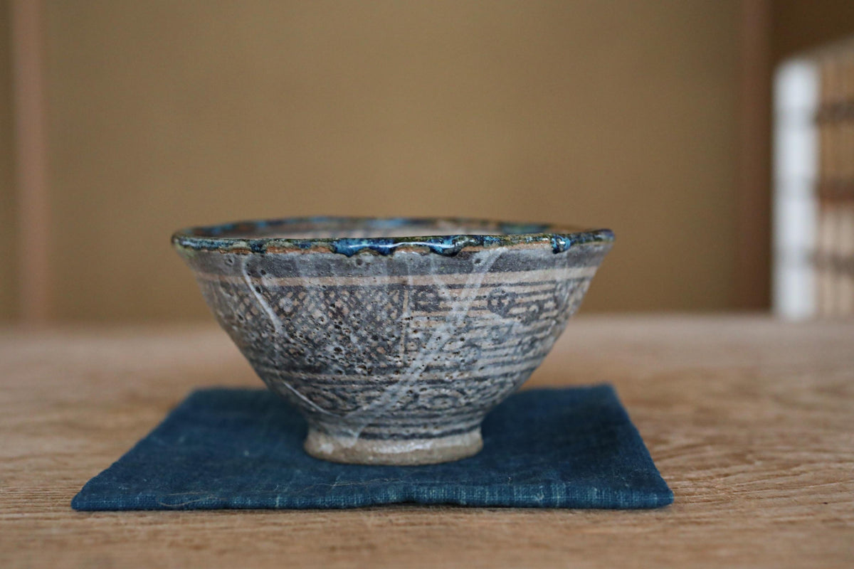 A ceramic bowl with a blue and white patterned design sits on a blue cloth on a wooden table.