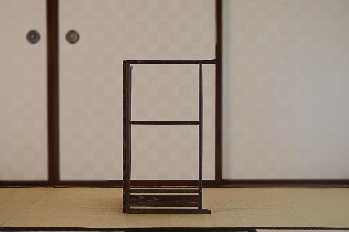 a wooden frame with a blank space in the center, standing on a tatami mat in a room with traditional Japanese-style sliding doors.