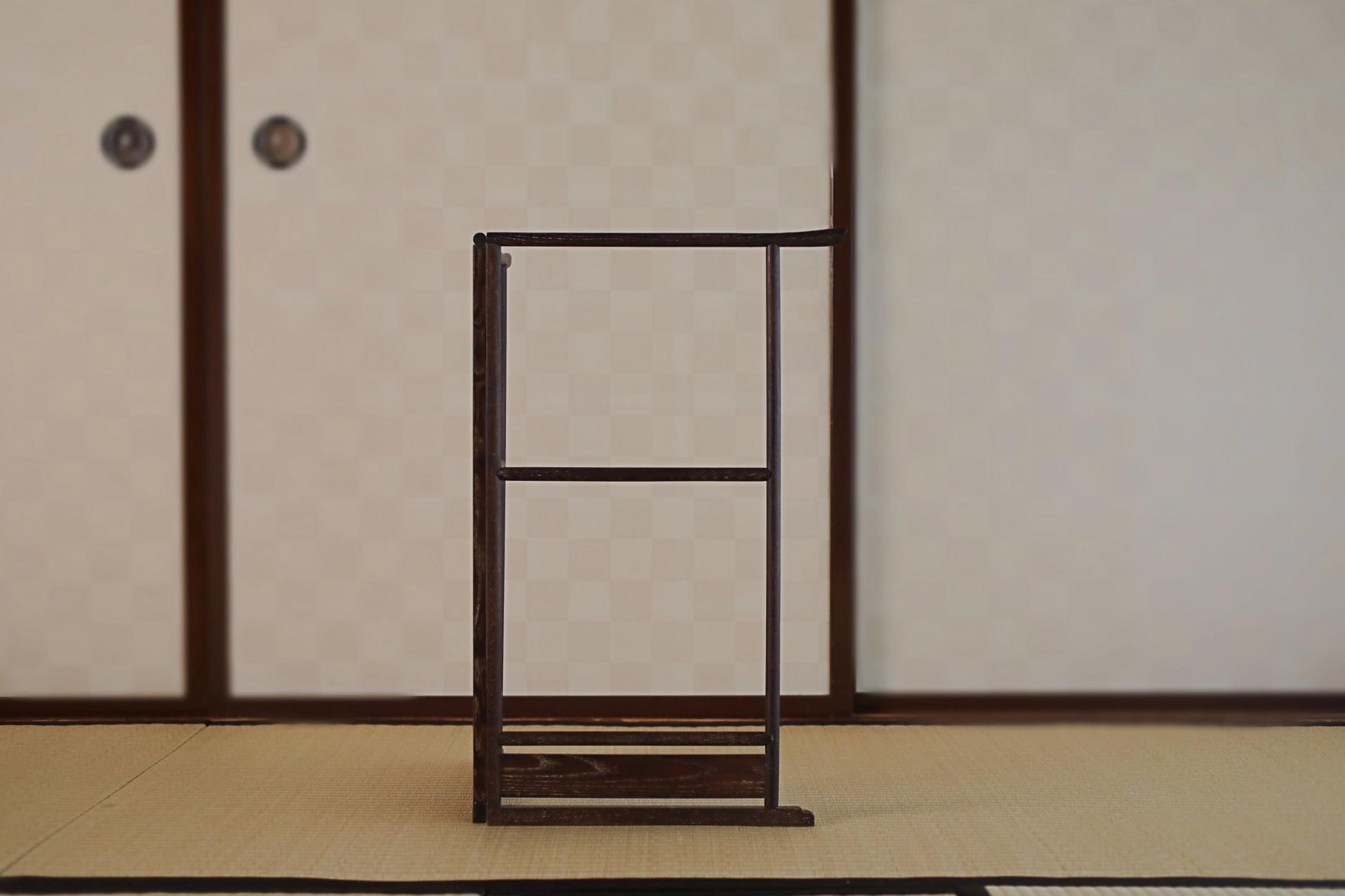 a wooden frame with a blank space in the center, standing on a tatami mat in a room with traditional Japanese-style sliding doors.