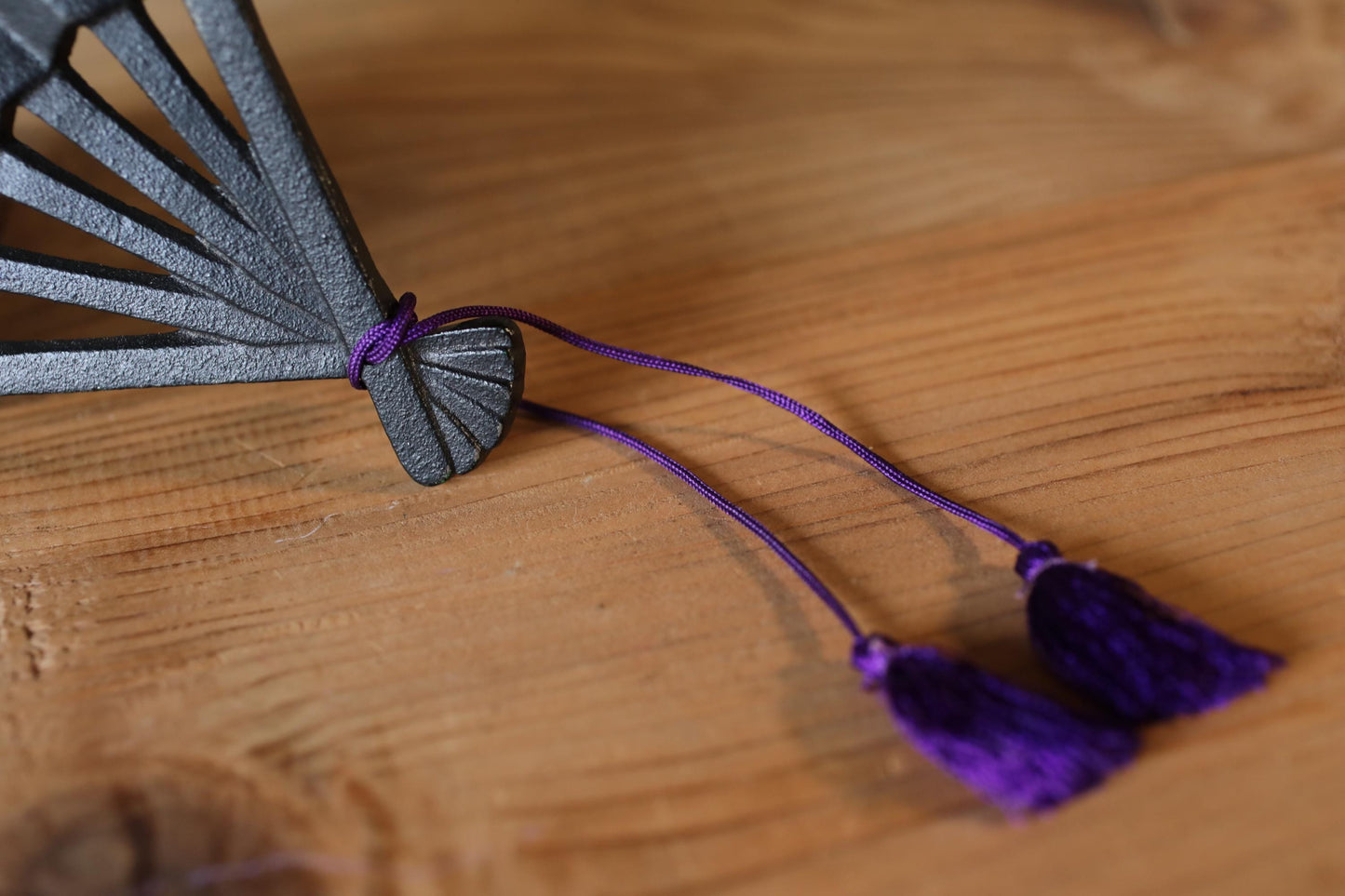 A close-up view of a decorative fan with purple tassels on a wooden surface.
