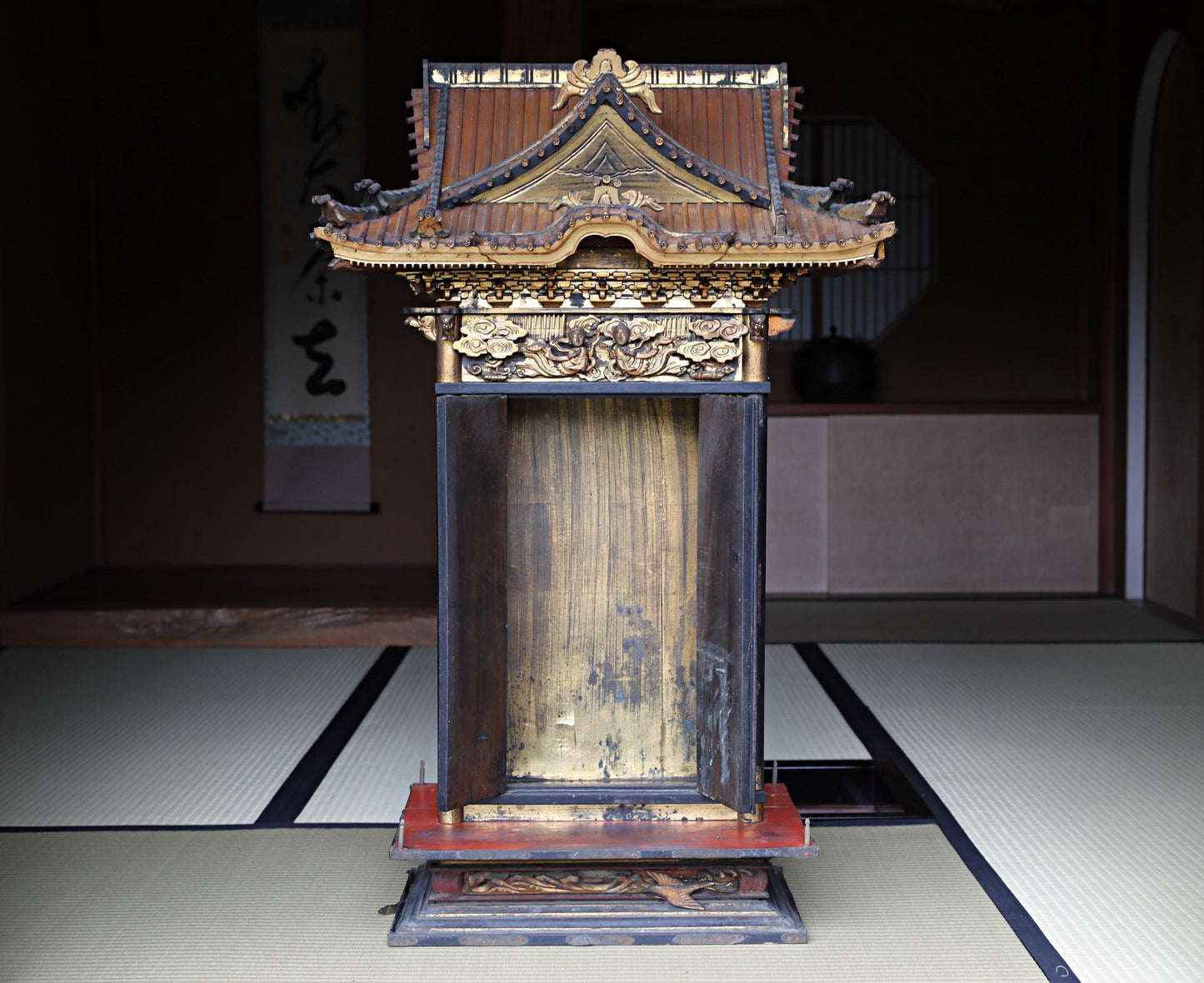 a traditional Japanese shrine with a wooden roof and intricate carvings, situated in a dimly lit room with tatami mats on the floor.