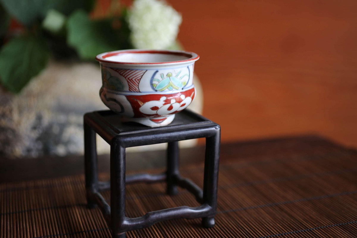 A small, colorful ceramic bowl is placed on a black metal stand on a wooden surface.