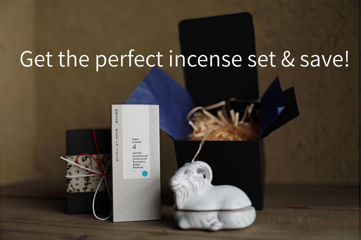 a set of incense sticks, a small ceramic figurine, and a black box with a blue lid, all placed on a wooden surface.