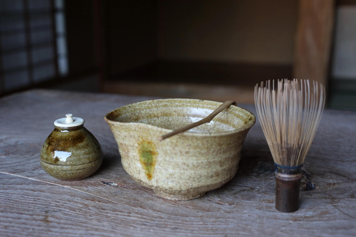 A ceramic bowl with a wooden spoon and a wooden whisk are placed on a wooden surface.