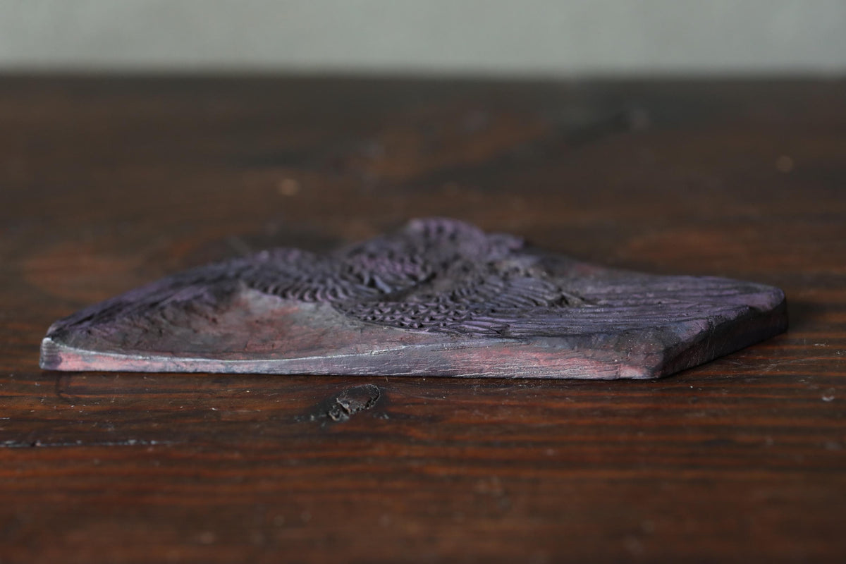 A close-up image of a dark purple, textured object, possibly a piece of wood or a stone, resting on a wooden surface.