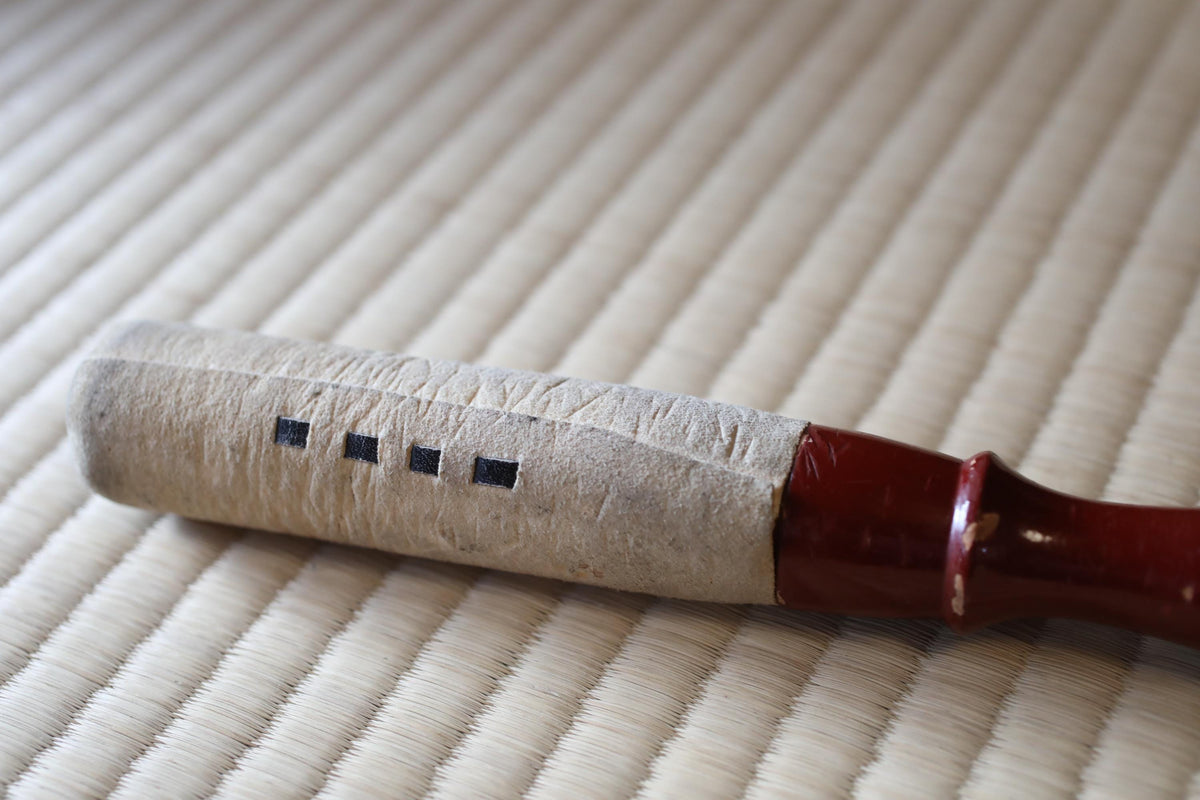 A close-up image of a wooden object with a red handle, resting on a woven surface.