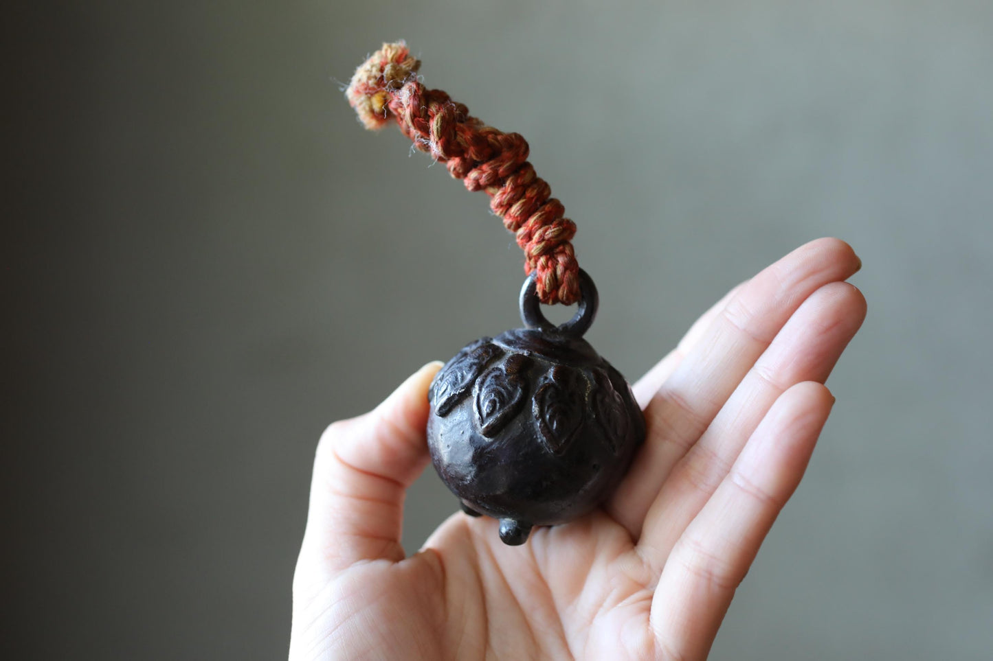 A hand holding a small, round, black object with a red string or cord attached to it.