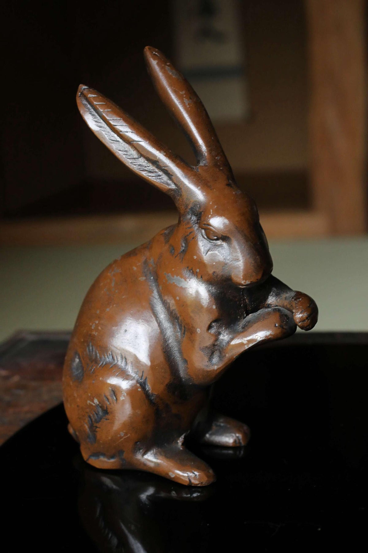 A bronze statue of a rabbit sitting on a black surface.