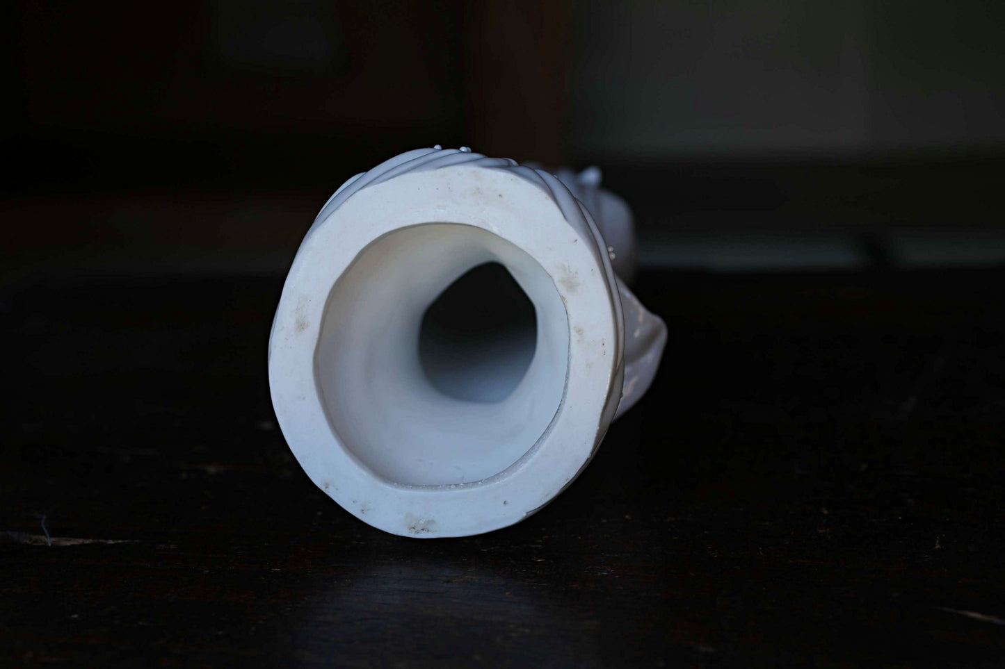 A white ceramic object with a circular opening, possibly a vase or sculpture, is shown against a dark background.