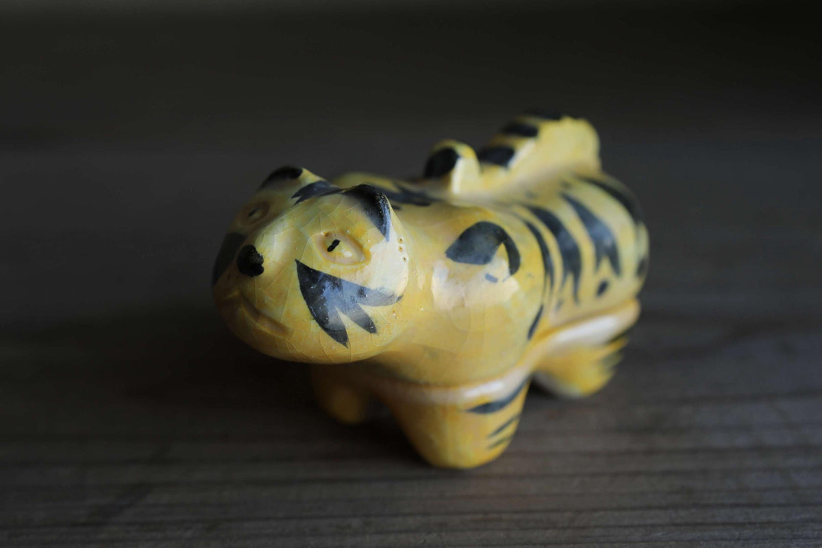 A yellow and black tiger figurine is sitting on a wooden surface.