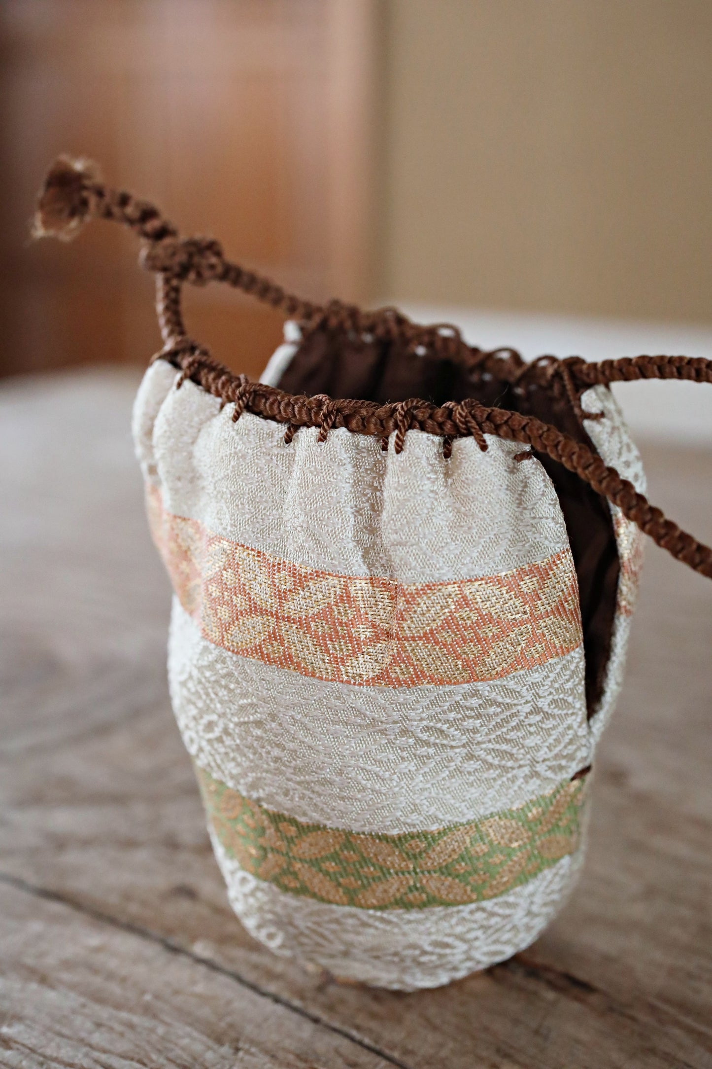 A white and brown woven pouch with a floral pattern sits on a wooden surface.