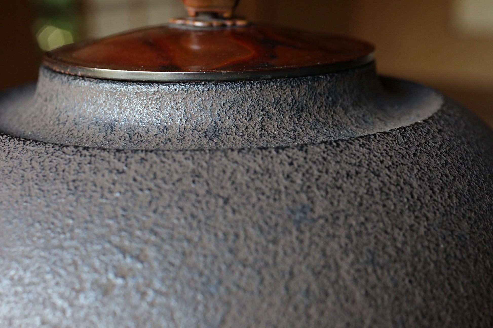 A close-up view of a textured gray ceramic object, possibly a vase or bowl, with a wooden lid or top.
