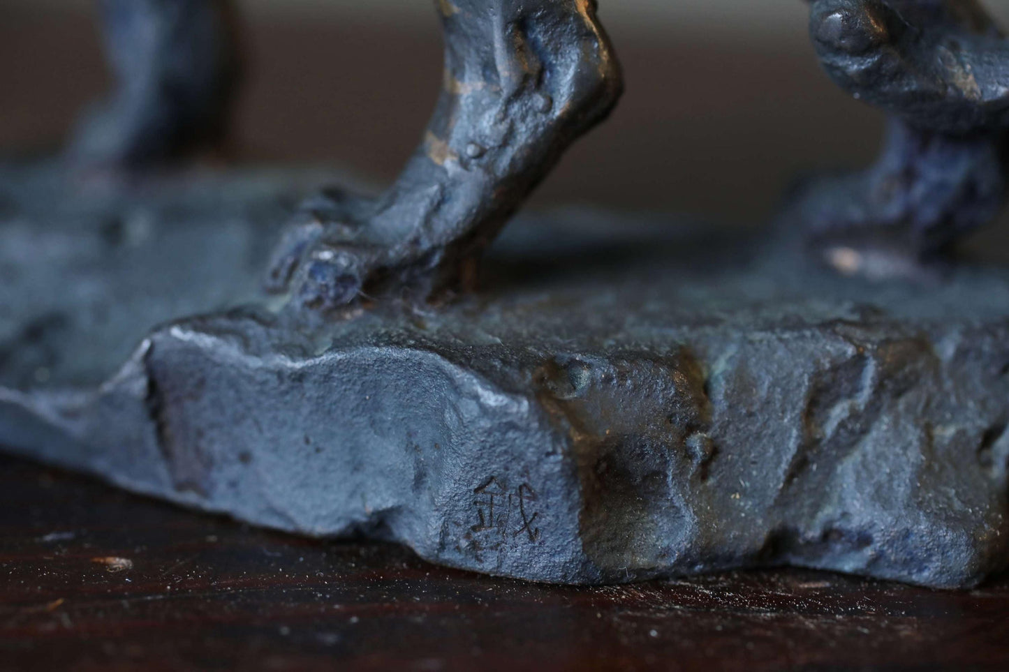 A close-up view of a dark-colored metal sculpture, possibly a piece of art or a decorative item, resting on a wooden surface.