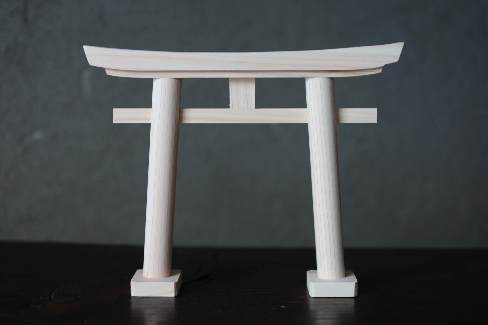 A wooden torii gate, a traditional Japanese gate, is shown against a dark background.