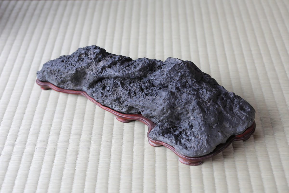 a large, dark gray rock sitting on a red base, placed on a white surface.