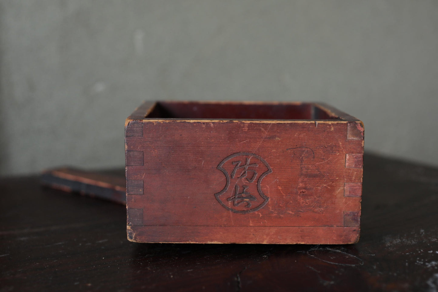 An old, weathered wooden box with a carved design on the front, sitting on a dark surface.