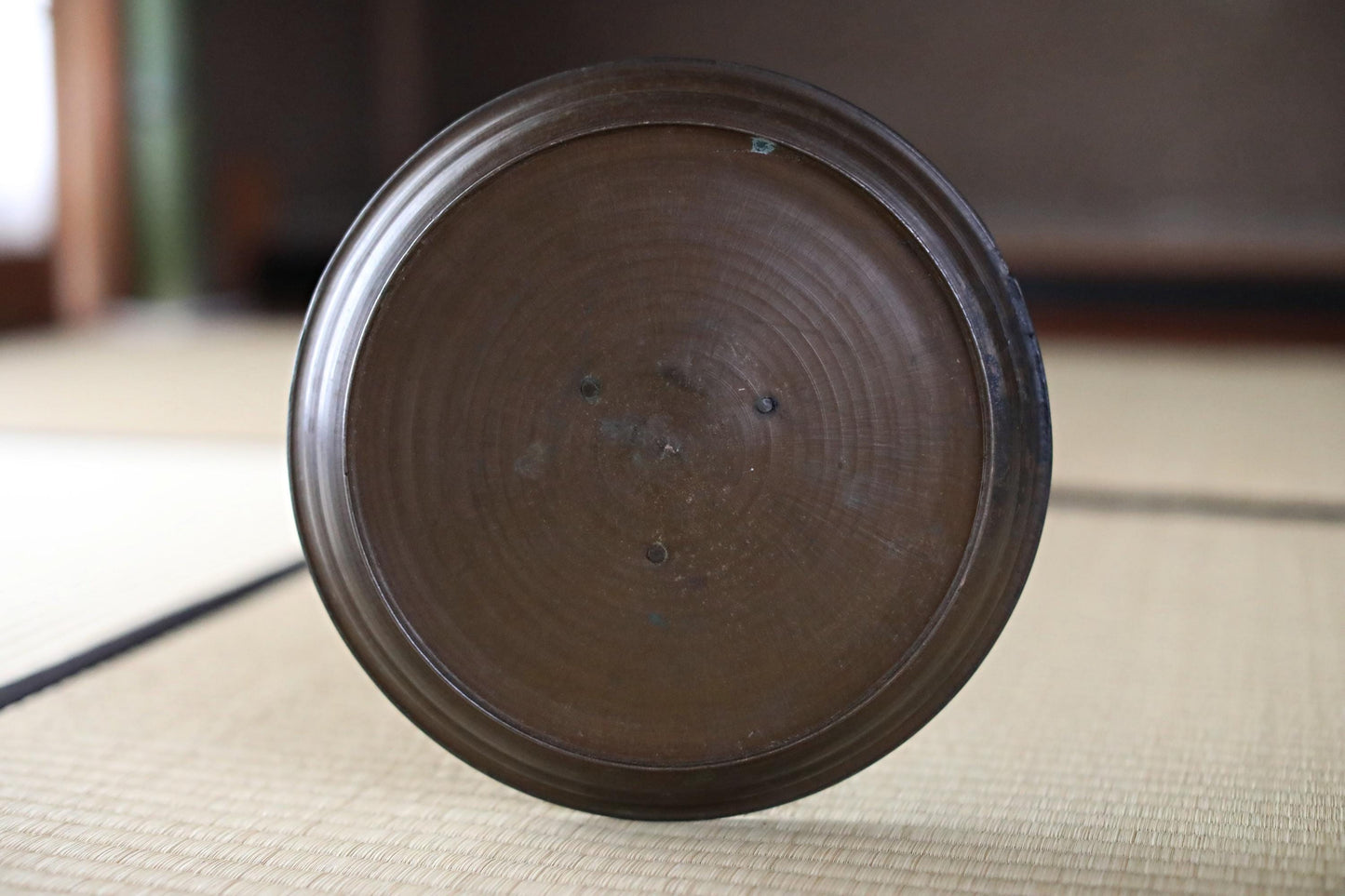 A close-up image of a dark brown, circular plate or bowl resting on a woven mat or surface.