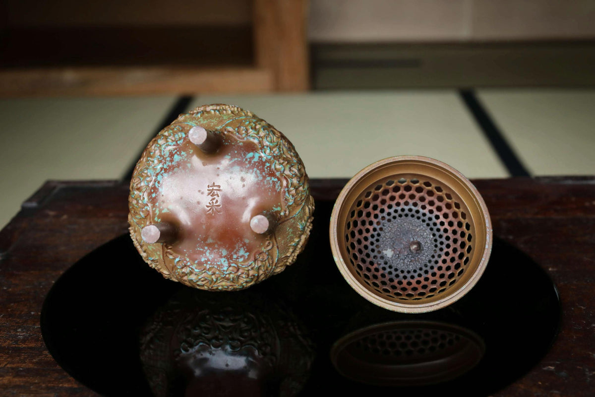 two ceramic objects, one with a floral design and the other with a perforated pattern, placed on a reflective surface.