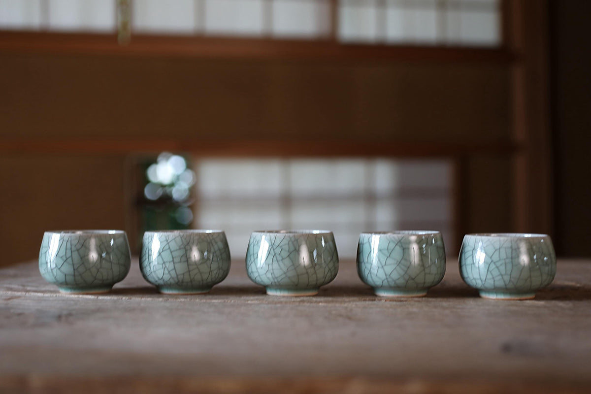 A row of five small, light blue ceramic cups or bowls arranged on a wooden surface.