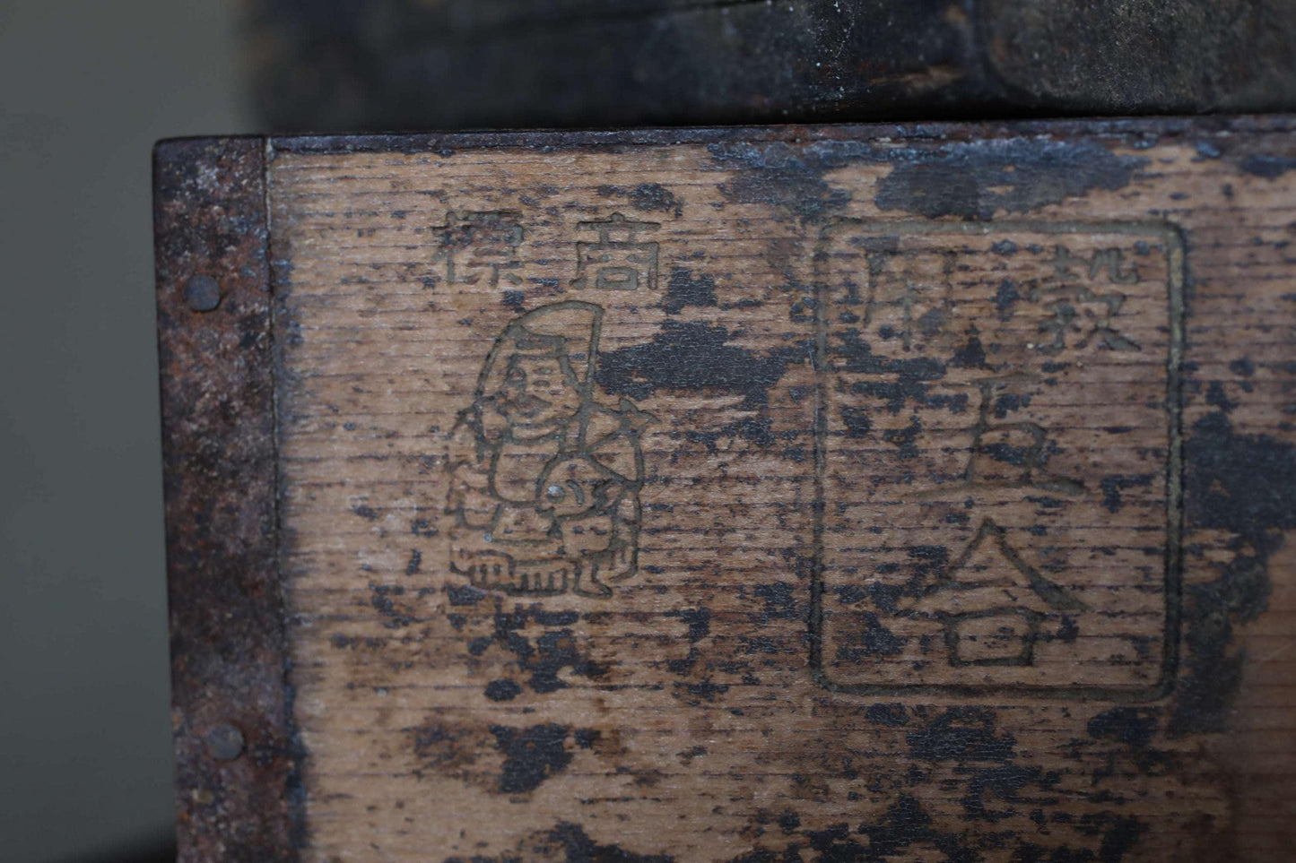 a close-up view of a weathered wooden surface with various markings and symbols, including a small figure and some text or symbols in a non-Latin script.