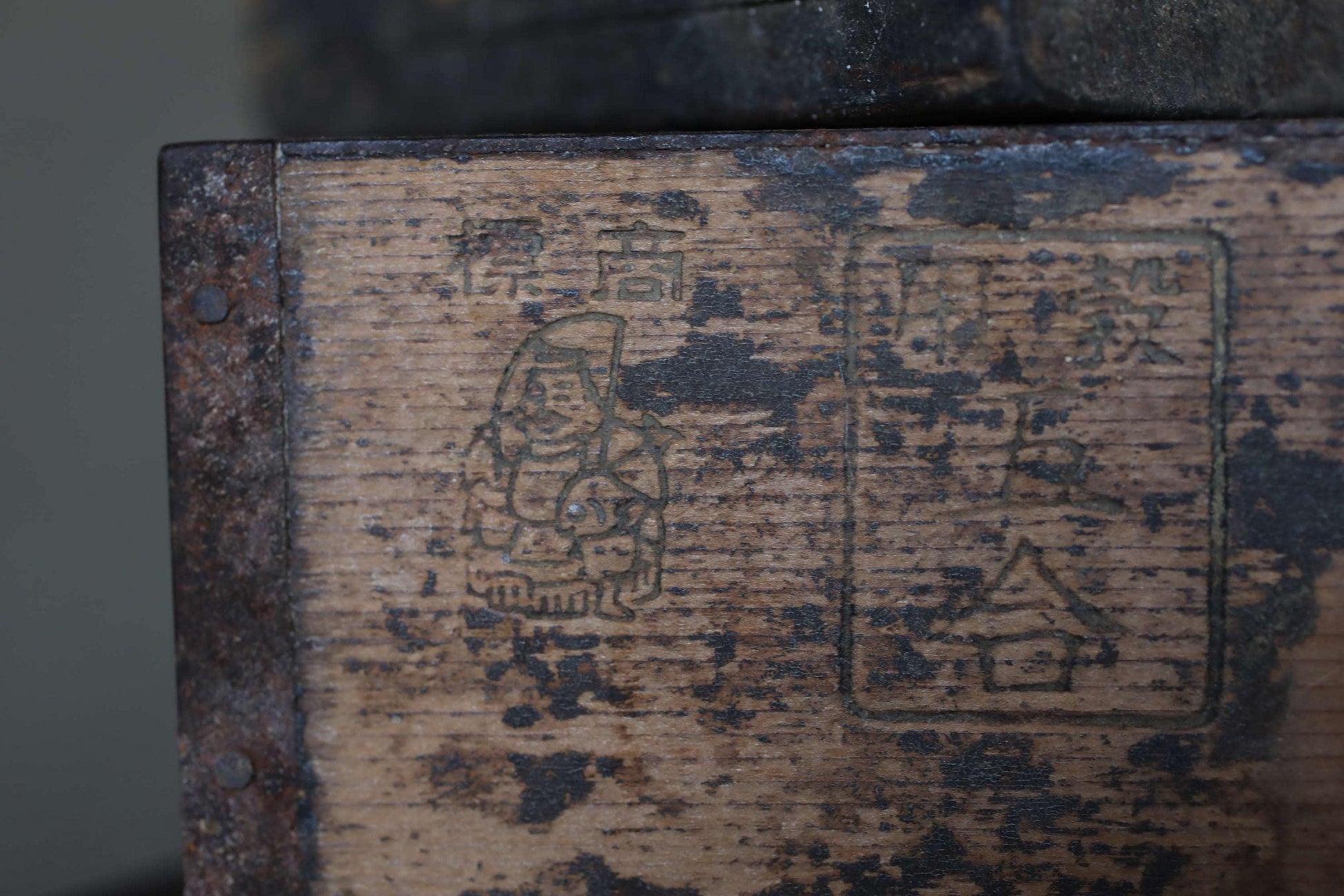 a close-up view of a weathered wooden surface with various markings and symbols, including a small figure and some text or symbols in a non-Latin script.