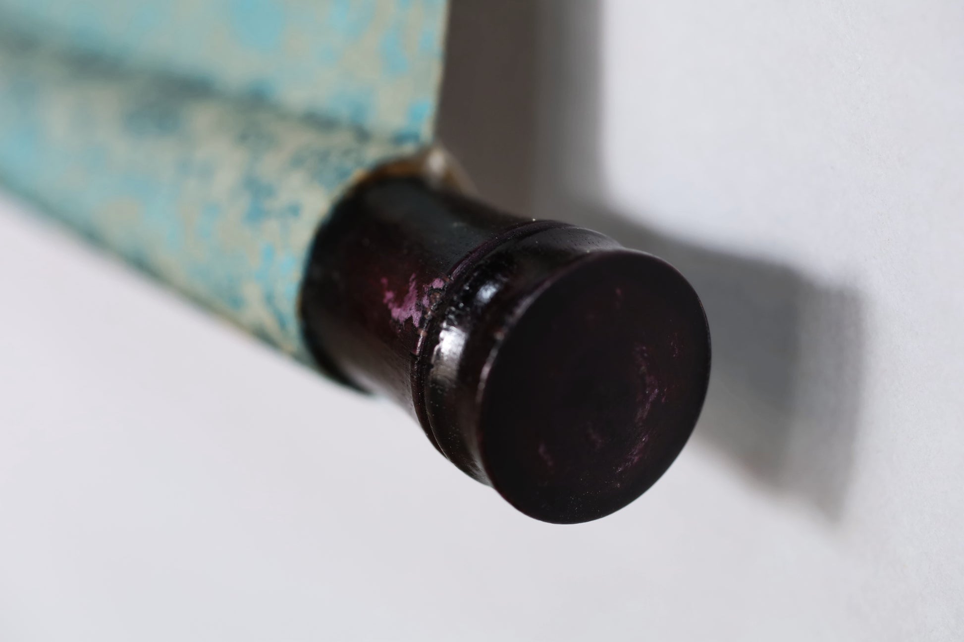 A close-up view of a dark-colored metal object, possibly a cap or handle, attached to a blue and white striped surface.