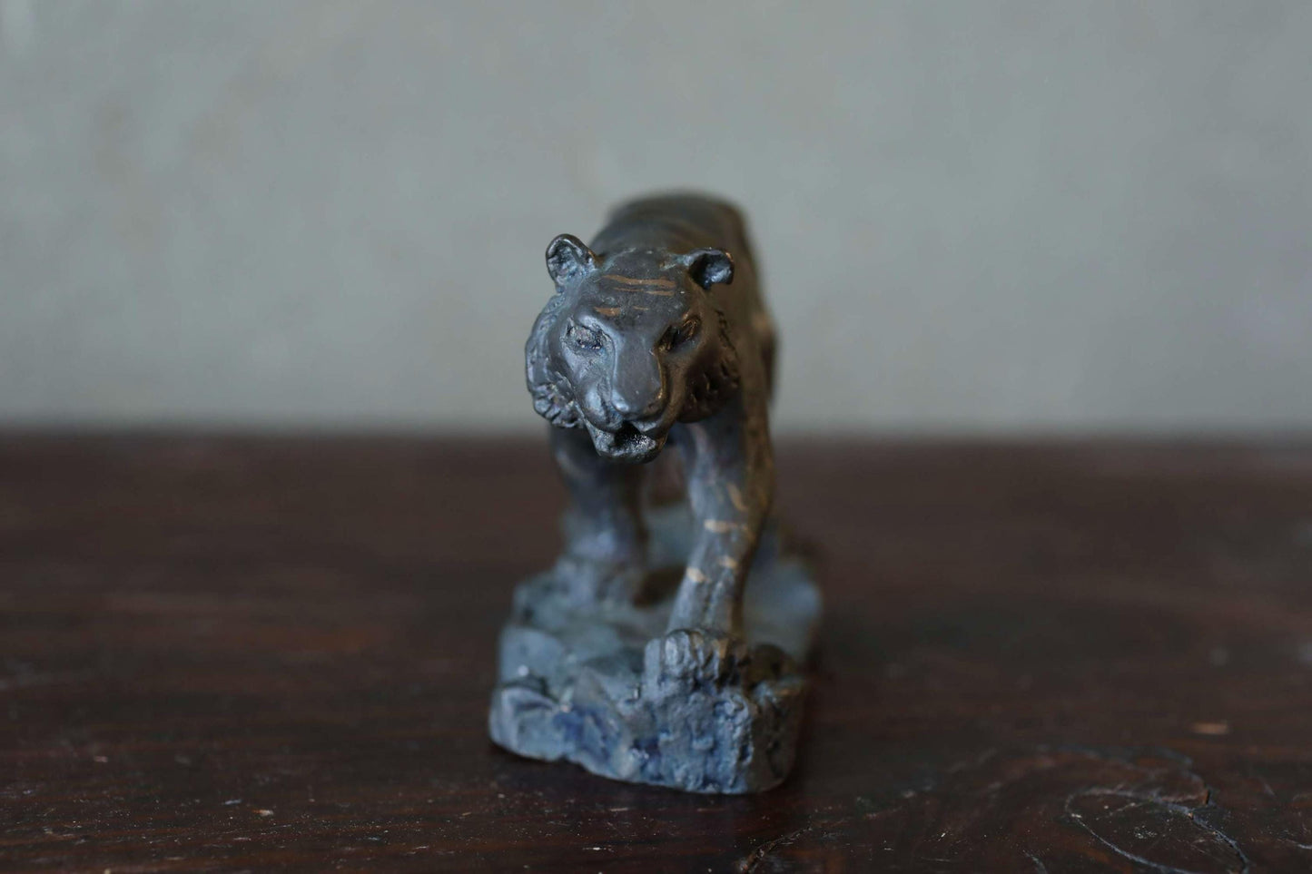 A small, dark-colored metal sculpture of a tiger-like animal, possibly a lion or a similar feline creature, is displayed on a wooden surface.