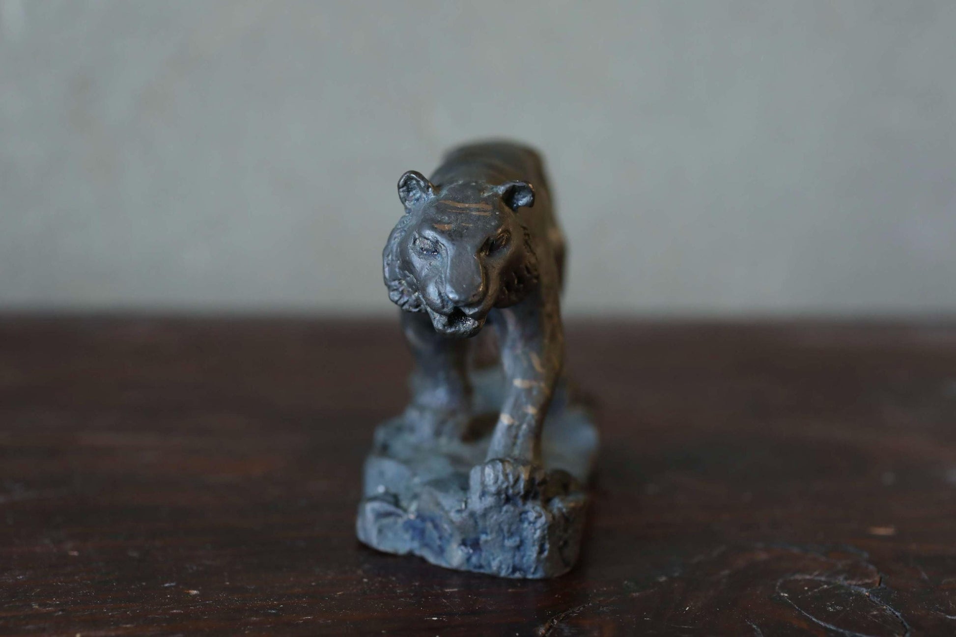 A small, dark-colored metal sculpture of a tiger-like animal, possibly a lion or a similar feline creature, is displayed on a wooden surface.