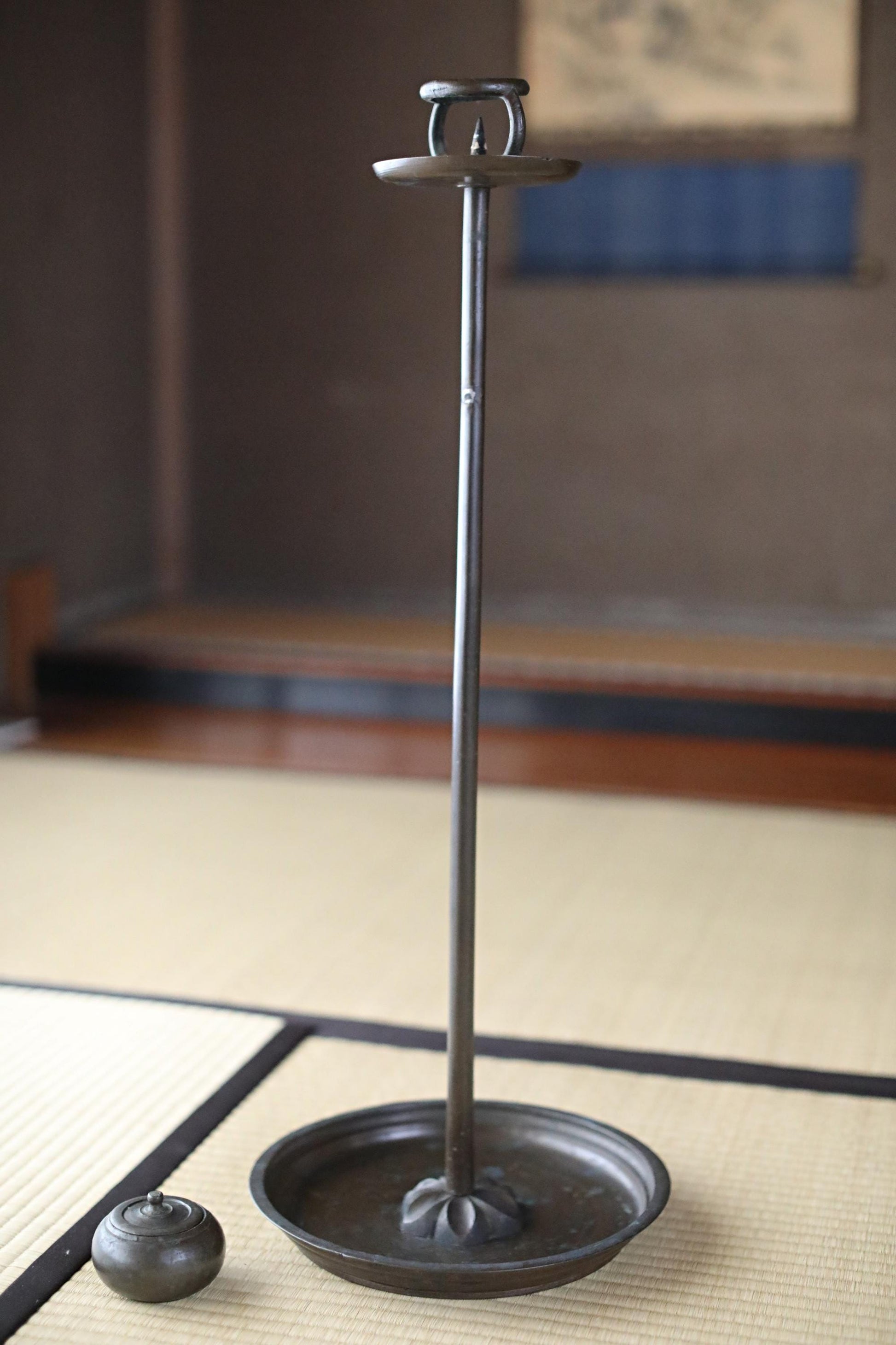 a tall, black metal candle holder with a round base, placed on a woven mat.
