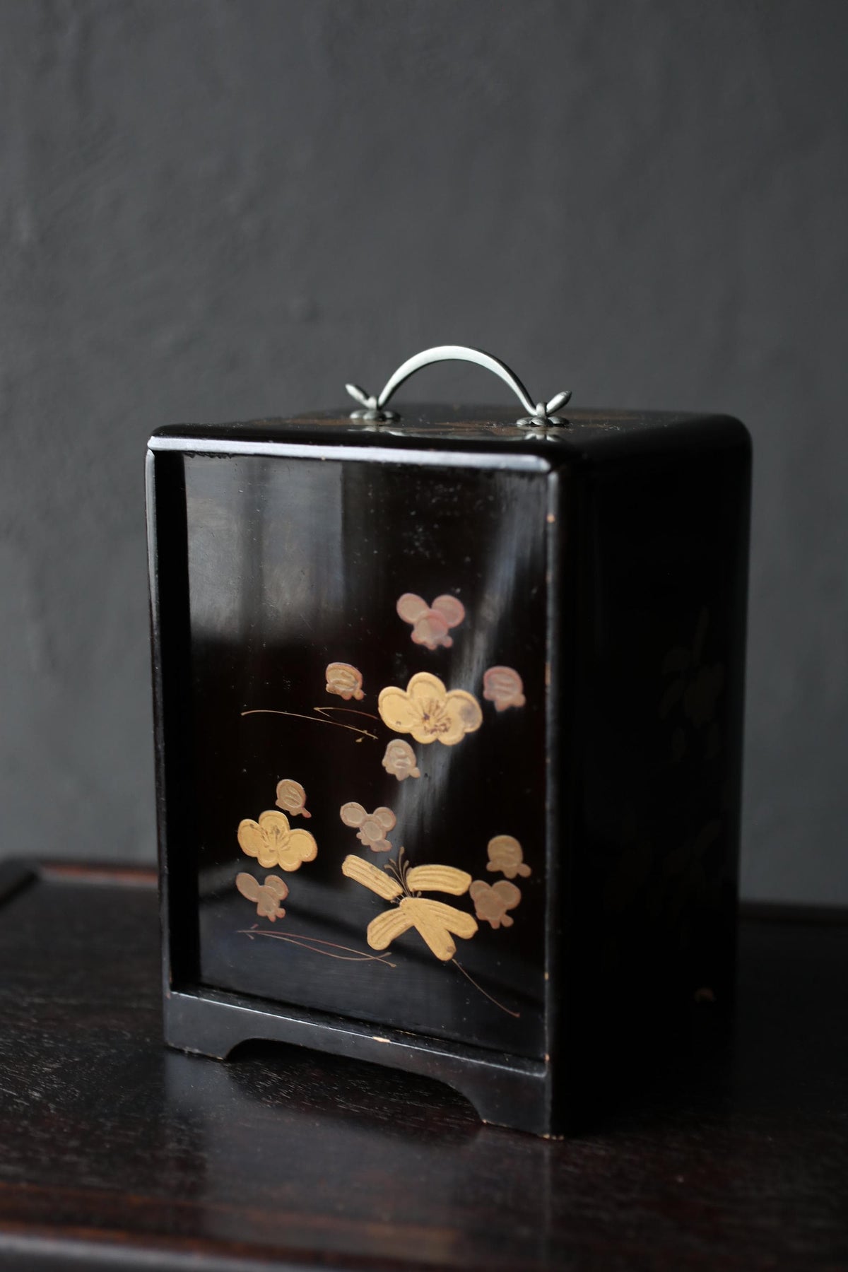 A black wooden box with a handle on top, featuring a floral design on its surface.