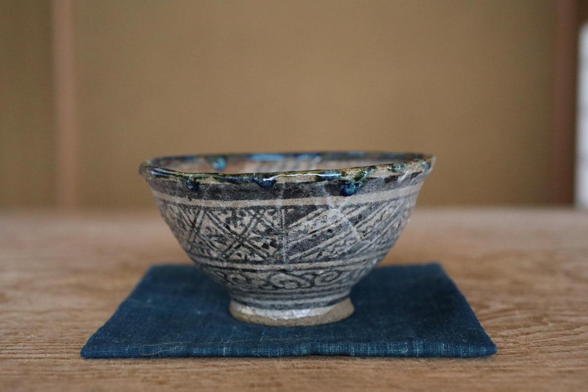 A ceramic bowl with a blue and white patterned design sits on a blue cloth on a wooden surface.