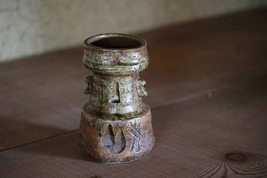 An old, weathered ceramic vase with a distinctive design sits on a wooden surface.