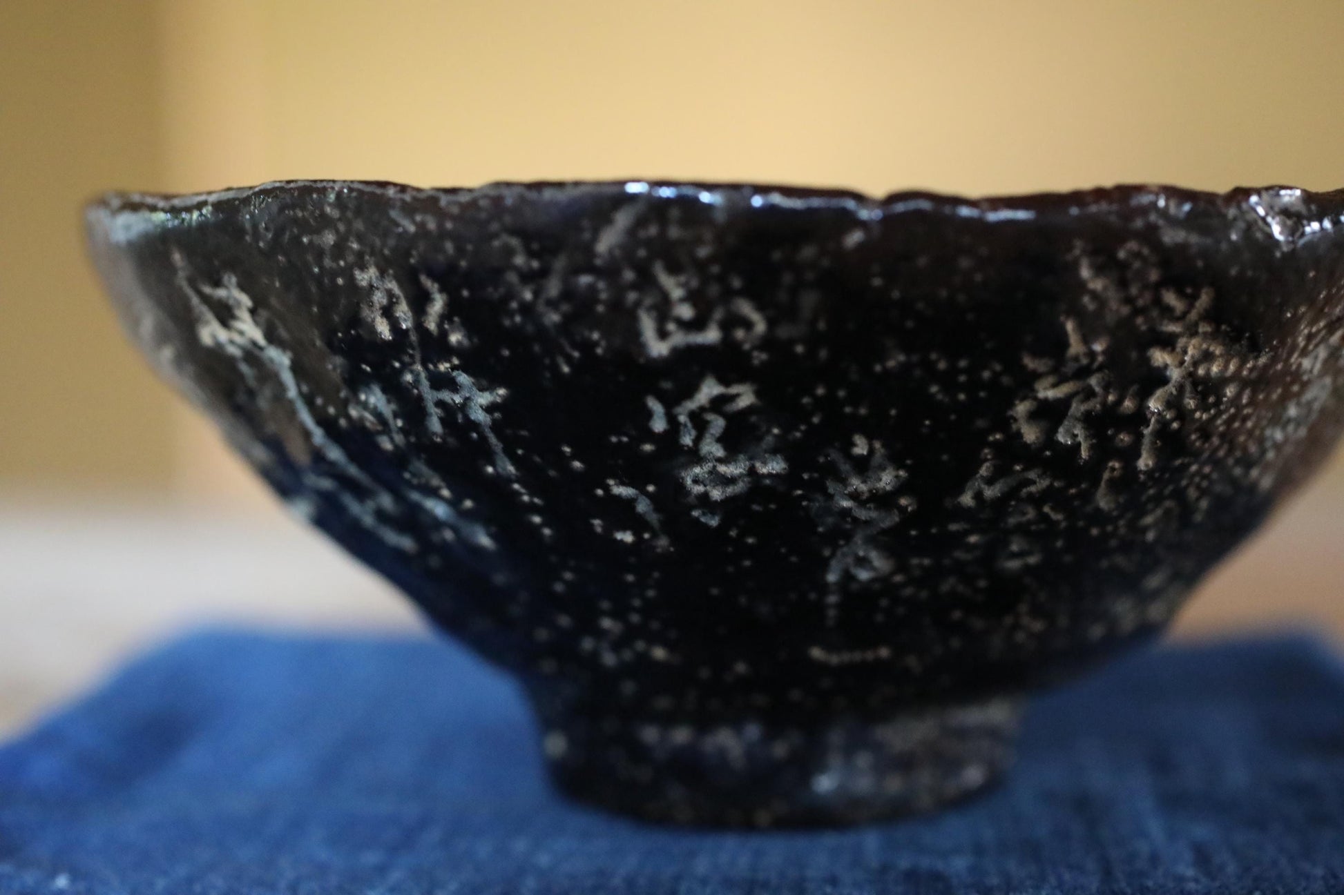 A close-up image of a black ceramic bowl with a speckled texture, resting on a blue cloth.