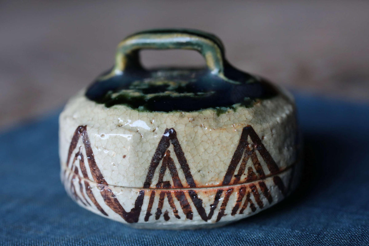A ceramic container with a handle and a decorative pattern on its surface, placed on a blue surface.