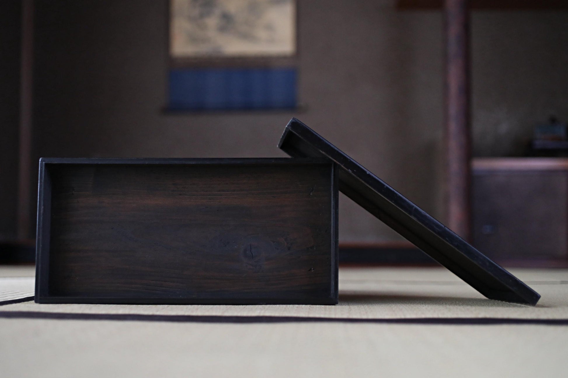 A dark wooden box rests on a beige surface, with a blurred background suggesting an indoor setting.