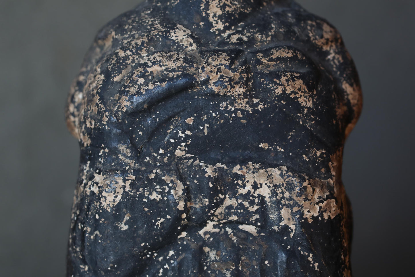 a close-up view of a weathered, black, and brown statue or sculpture with a textured, aged appearance.