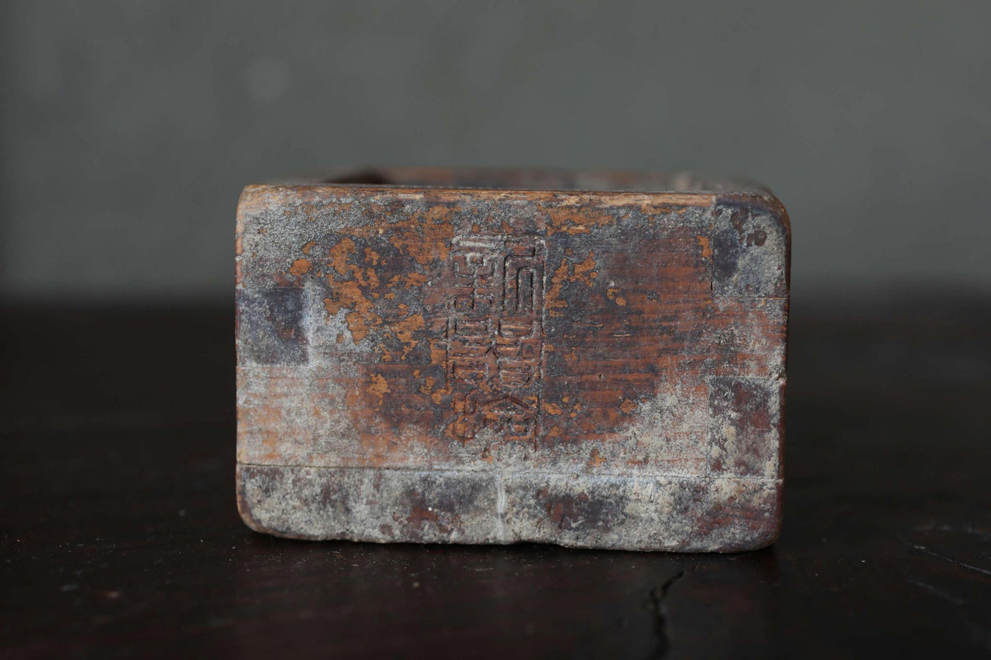 An old, weathered metal object with a faded, rust-colored surface, sitting on a dark surface.