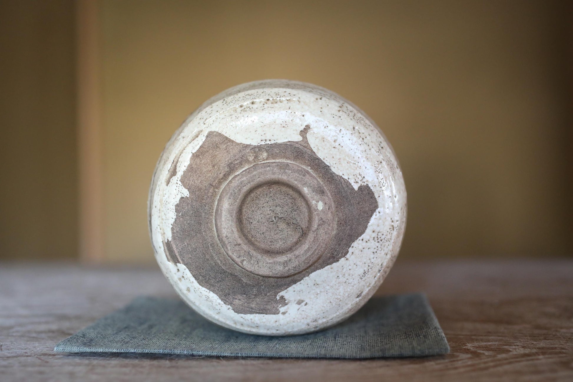 A white ceramic bowl with a brown speckled pattern sits on a blue cloth on a wooden surface.