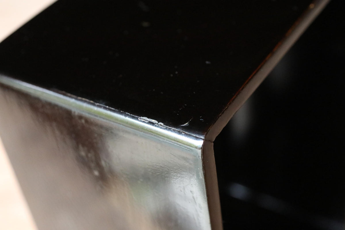 a close-up view of a black, shiny surface, possibly a metal or glass object, with a slight reflection visible on its surface.